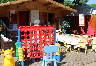 Zona de juegos infantil al aire libre con casita, sillas, mesa y juego gigante en Camping Paradis Family des Issoux.