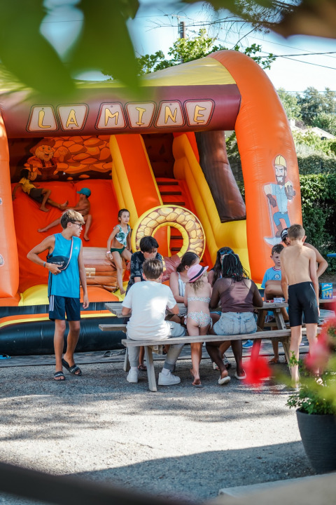 Kids play and sit at a picnic table in front of an inflatable slide at Flower Camping Provence Vallée, France.