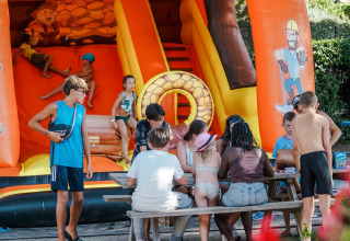 Kids play and sit at a picnic table in front of an inflatable slide at Flower Camping Provence Vallée, France.