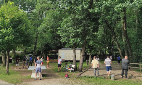 Holiday park scene with people playing table tennis and pétanque at Camping Le Savoy, France, among trees.