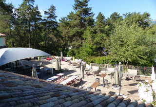 Terrasse extérieure du Flower Camping la Pinède, parc de vacances en Auvergne-Rhône-Alpes, France, entourée d’arbres.