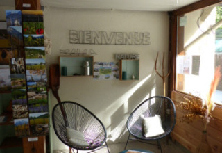 Zona lounge luminosa e moderna con sedie e cartoline a Flower Camping la Pinède, Auvergne-Rhône-Alpes, Francia.