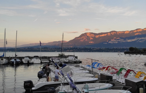 Barche e pedalò ormeggiati vicino a un lago a Challes les Eaux, Francia, con montagne illuminate dal tramonto.