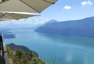 View of a serene lake and surrounding mountains from a terrace with umbrellas near Challes les Eaux, France.