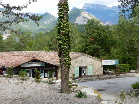 Vue sur la réception et le restaurant du Flower Camping la Pinède en Auvergne-Rhône-Alpes, entourés de montagnes verdoyantes.