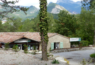 Vista della reception e del ristorante del Flower Camping la Pinède in Auvergne-Rhône-Alpes, circondati da montagne.