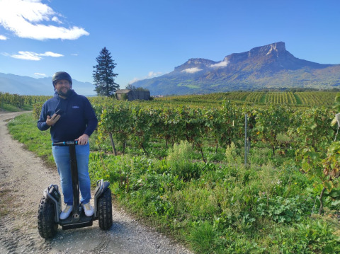 Mand på en Segway kører langs en vinmark med bjerge i baggrunden i Auvergne-Rhône-Alpes, Frankrig.