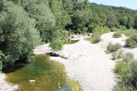 Vista de un río poco profundo rodeado de árboles y grava en Camping Paradis Family des Issoux, Francia.