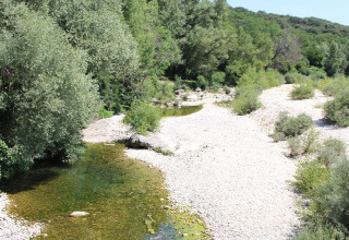 View of a shallow river with gravel banks and green trees at Camping Paradis Family des Issoux in France.