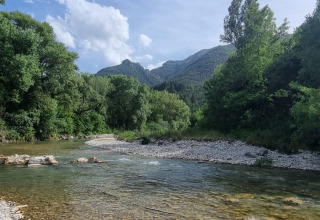 Flod med stenbred, grønne træer og bjerge i baggrunden ved Flower Camping la Pinède, Auvergne-Rhône-Alpes.