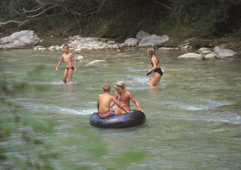 Børn leger i en lav flod med en badering på Flower Camping la Pinède i Auvergne-Rhône-Alpes, Frankrig.