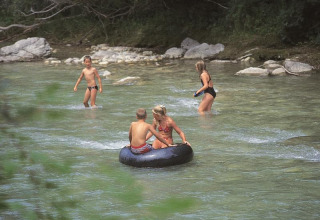Børn leger i en lav flod med en badering på Flower Camping la Pinède i Auvergne-Rhône-Alpes, Frankrig.