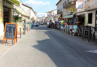 Vista stradale a Lalevade d'Ardèche, Francia, con caffè all'aperto, negozi locali e persone sedute.