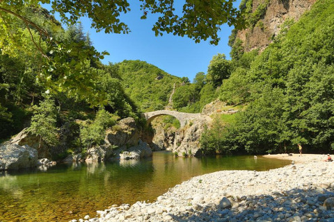 Stone bridge over a river surrounded by green hills near Lalevade d'Ardèche, Auvergne-Rhône-Alpes, France.