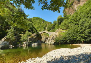 Stone bridge over a river surrounded by green hills near Lalevade d'Ardèche, Auvergne-Rhône-Alpes, France.
