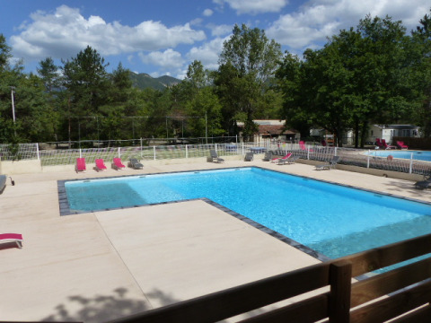 Piscina all'aperto con lettini e alberi circostanti al Flower Camping la Pinède in Auvergne-Rhône-Alpes, Francia.