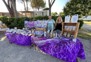 Ein Paar steht hinter einem Marktstand mit Lavendelprodukten auf dem Flower Camping Provence Vallée in Frankreich.