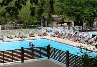 Outdoor swimming pool with sun loungers and people enjoying the sun at Flower Camping la Pinède holiday park.