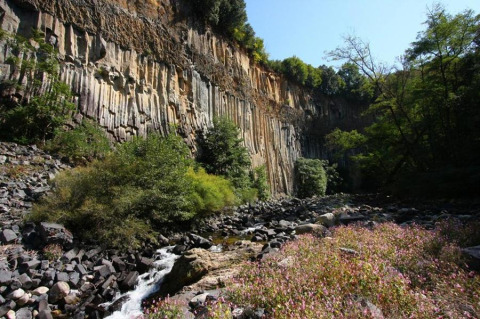 Basalt cliff with a flowing creek and wildflowers at Camping Paradis Family des Issoux holiday park, France.