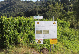 Hinweisschilder, Warnhinweise und grüne Büsche im Camping Paradis Family des Issoux, Auvergne-Rhône-Alpes, Frankreich.