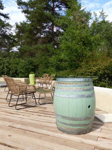 Terrasse extérieure avec table tonneau verte, chaises en osier et arbres dans un parc de vacances en Auvergne-Rhône-Alpes.