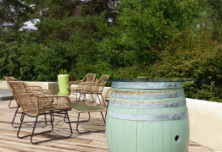 Udendørs terrasse med grøn vintønde, fletstole og grønne træer i baggrunden i Auvergne-Rhône-Alpes.