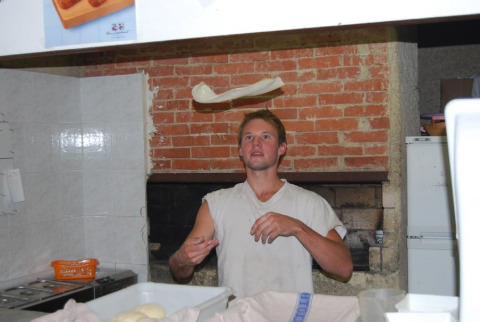 A baker tosses pizza dough in a kitchen with a brick wall at Flower Camping la Pinède in France.