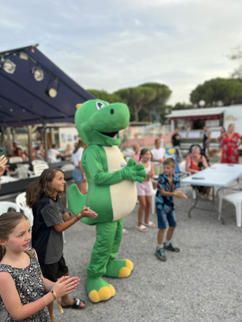 Bambini applaudono accanto a una mascotte dinosauro presso Flower Camping Provence Vallée, Francia del Sud.
