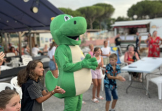 Kinder klatschen neben einer Person im Dinosaurierkostüm bei Flower Camping Provence Vallée, Frankreich.
