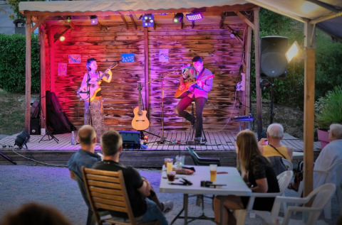 Livemusik auf einer kleinen Bühne im Flower Camping Provence Vallée, Frankreich, vor entspanntem, sitzendem Publikum.