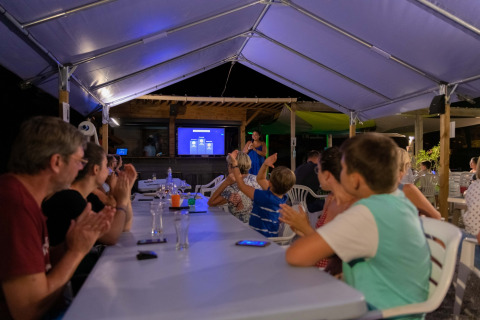 Guests seated under a canopy at Flower Camping Provence Vallée, France, enjoying evening entertainment.