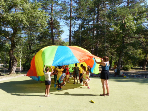 Des enfants jouent avec un parachute coloré en plein air au Flower Camping la Pinède en Auvergne-Rhône-Alpes, France.