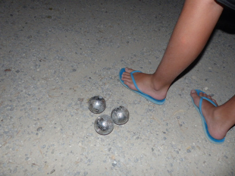 Personne en tongs bleues près de quatre boules métalliques sur du gravier à Flower Camping la Pinède, Auvergne-Rhône-Alpes.