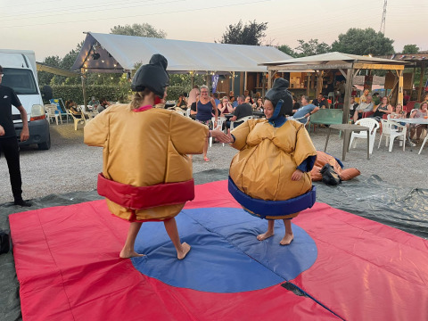 Zwei Personen im Sumo-Kostüm ringen auf einer Matte, umgeben von Zuschauern in einem Ferienpark.