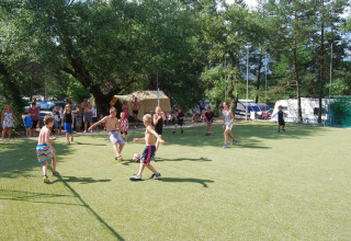 Children play soccer on the field at Flower Camping la Pinède, with adults and families watching behind them.