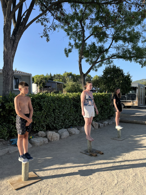 Tres personas se equilibran sobre postes de madera en un parque de vacaciones en Provenza, Francia, bajo el sol.