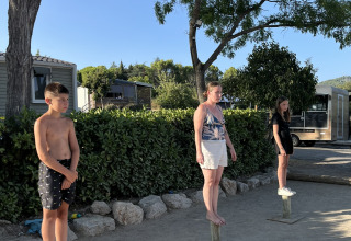 Tre persone in equilibrio su pali di legno in un campeggio in Provenza-Alpi-Costa Azzurra, Francia, sotto il sole.