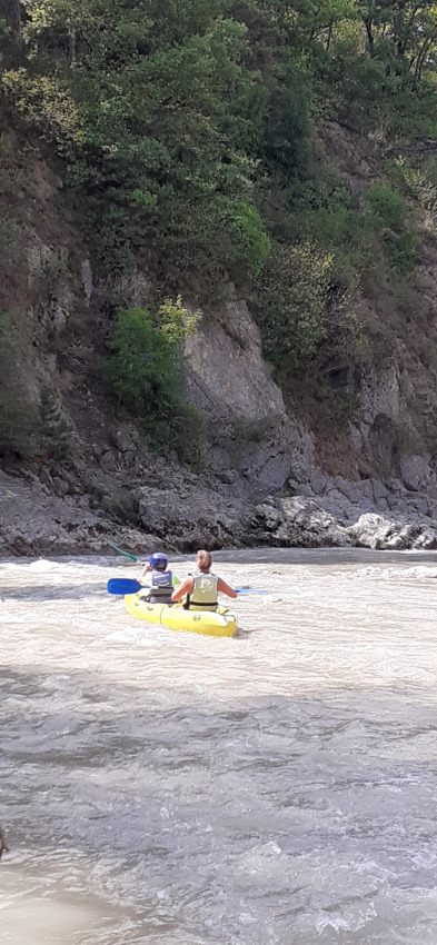 Deux personnes pagaient dans un kayak jaune sur une rivière bordée de falaises et de verdure en France.