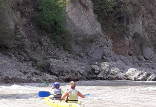 Deux personnes pagaient dans un kayak jaune sur une rivière bordée de falaises et de verdure en France.