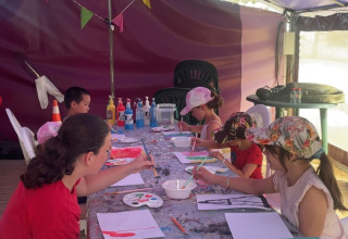 Enfants et adultes peignent ensemble à une longue table sous une tente au Flower Camping Provence Vallée.