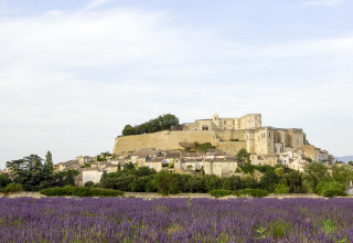 En udsigt over et lavendelfelt med en historisk by og slot i baggrunden i Auvergne-Rhône-Alpes, Frankrig.