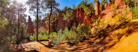 Panoramic view of ochre cliffs and pine trees near Manosque, Provence-Alpes-Côte d’Azur, France, on a sunny day.