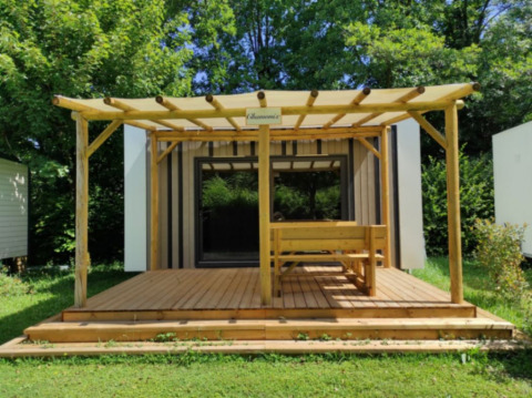 Cabaña de glamping moderna con terraza y pérgola de madera, en un entorno natural lleno de vegetación.