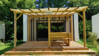 Una moderna casetta per glamping con terrazza e pergolato in legno, immersa nel verde della natura.