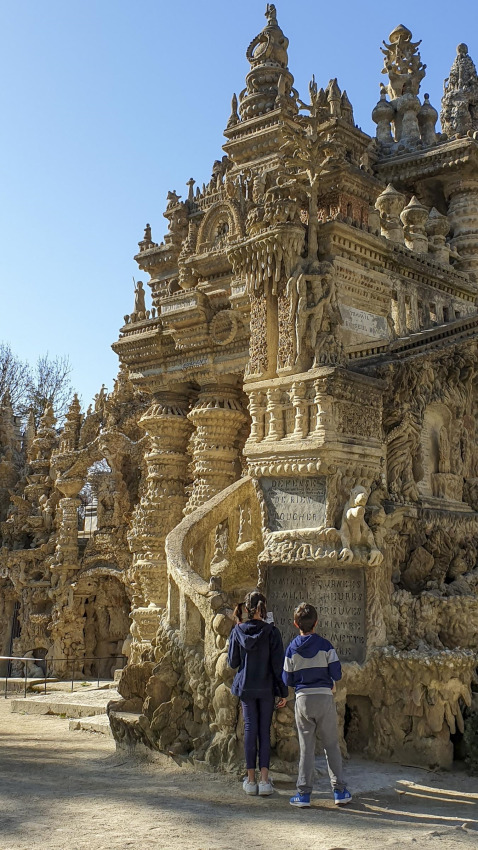 Two children admire an intricate stone structure in sunlight at Flower Camping la Pinède, France.