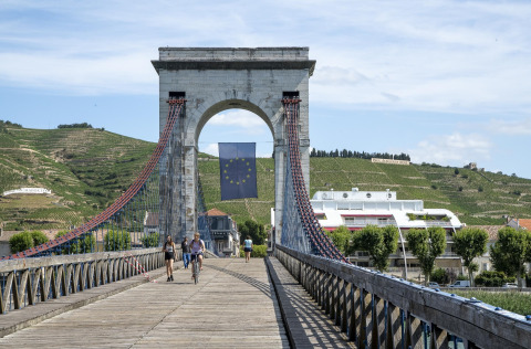 Persone che camminano e vanno in bicicletta su un ponte sospeso con bandiera UE in Auvergne-Rhône-Alpes, Francia.