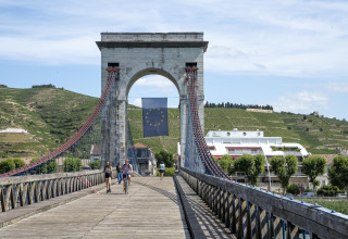 People walking and cycling on a suspension bridge with the EU flag in Auvergne-Rhône-Alpes, France.