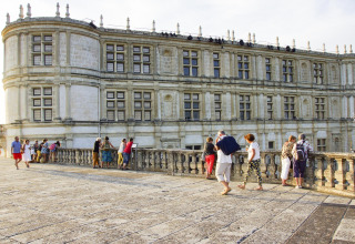 Visitatori passeggiano sulla terrazza di un castello storico a Flower Camping la Pinède, Auvergne-Rhône-Alpes, Francia.