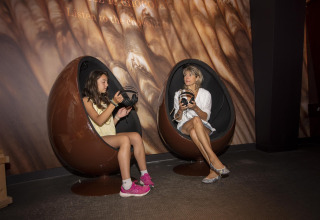 Two people sit in egg-shaped chairs holding headphones at Flower Camping la Pinède in France.