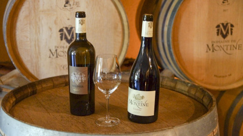 Dos botellas de vino Domaine de Montine y una copa sobre un barril en Flower Camping la Pinède, Auvergne-Rhône-Alpes.
